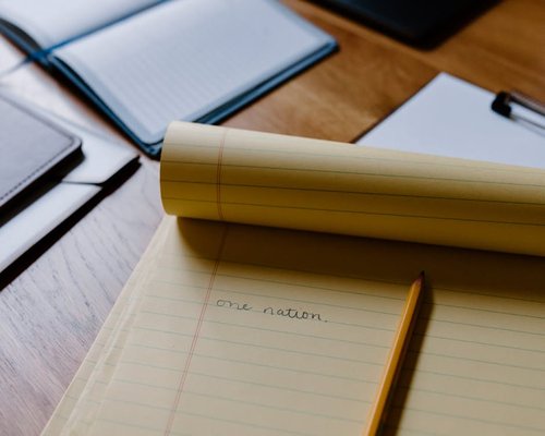 A well lit desk surface with open papers, pencils and notes near an office window frame